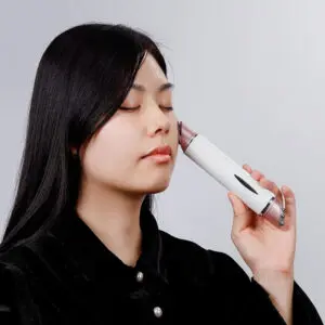 Mulher com os olhos cerrados segurando um dispositivo eletrônico de cuidado com a pele contra a sua pele.