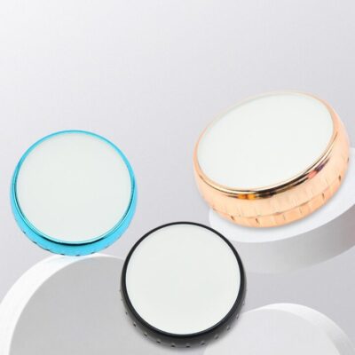 Three round compact mirrors with different colored edges—blue, rose gold, and black—placed on a gray background with white circular stands.